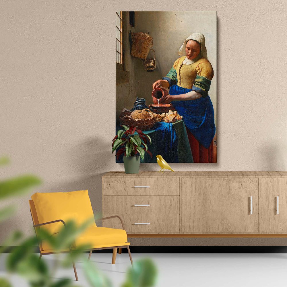 Classic artwork The Milkmaid by Johannes Vermeer depicts a woman standing by a table pouring milk into a bowl, with bread, ceramic vessels, and a basket hanging on the wall, bathed in soft sunlight streaming through a nearby window.