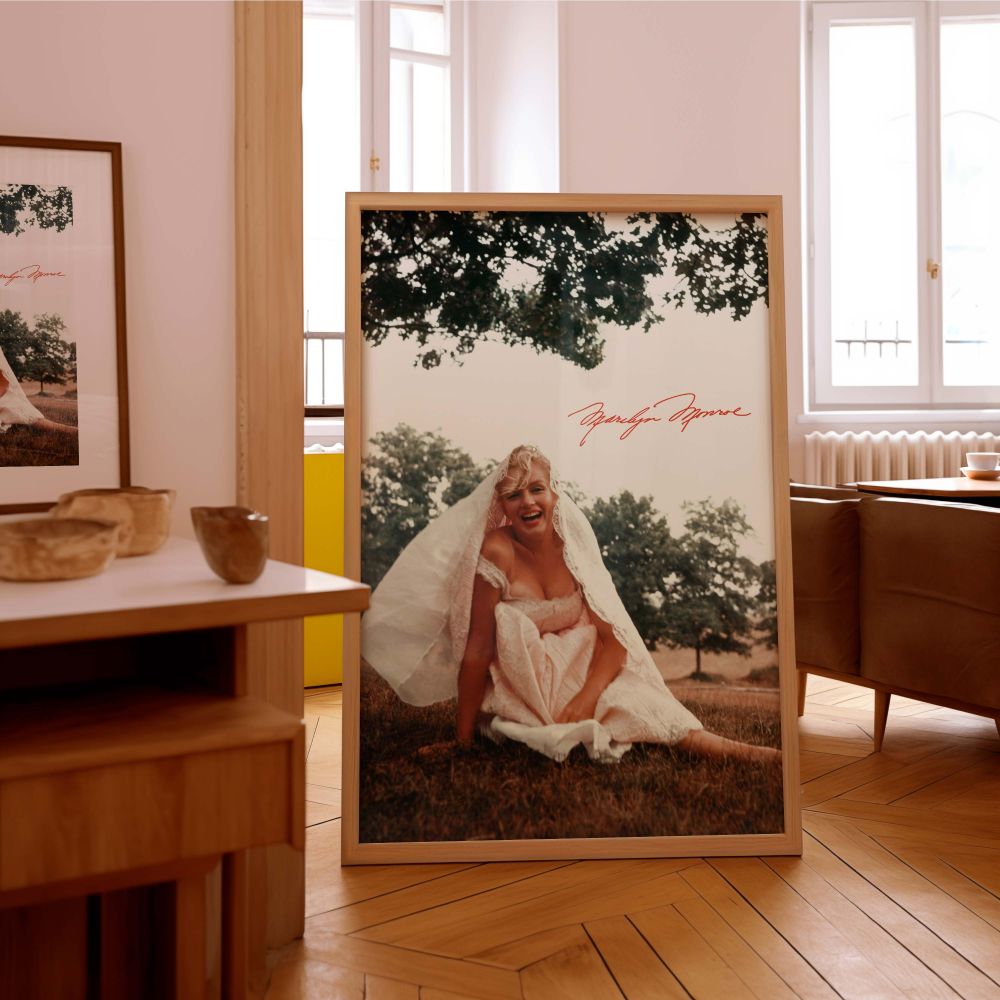 This Monroe wall print showcases her elegance and playfulness in a white dress sitting on the grass in an outdoor scene great for retro decor bridal-themed prints and collectors of classic film era photographs looking for unique portraits.
