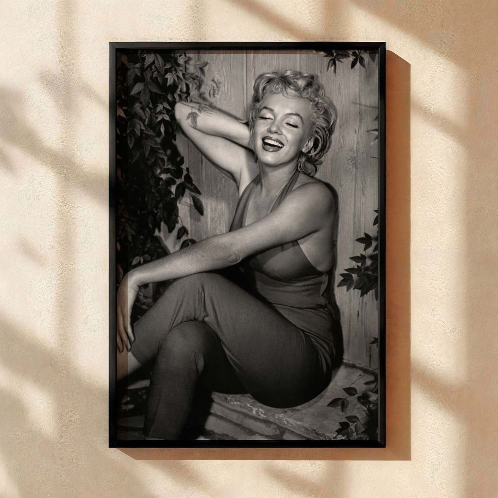 Joyful and relaxed Marilyn Monroe is captured mid-laughter in a black and white photo wearing her famous red jumpsuit surrounded by leaves making it an ideal vintage wall art piece for retro home styling and fans of classic Hollywood photography.