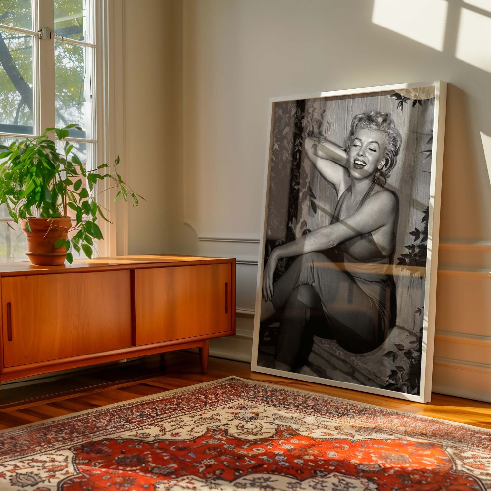 Classic Hollywood star Marilyn Monroe is seen laughing naturally in this vintage photograph seated in her red jumpsuit surrounded by leaves perfect for fans of 1950s photography iconic actress portraits and nostalgic black and white prints.