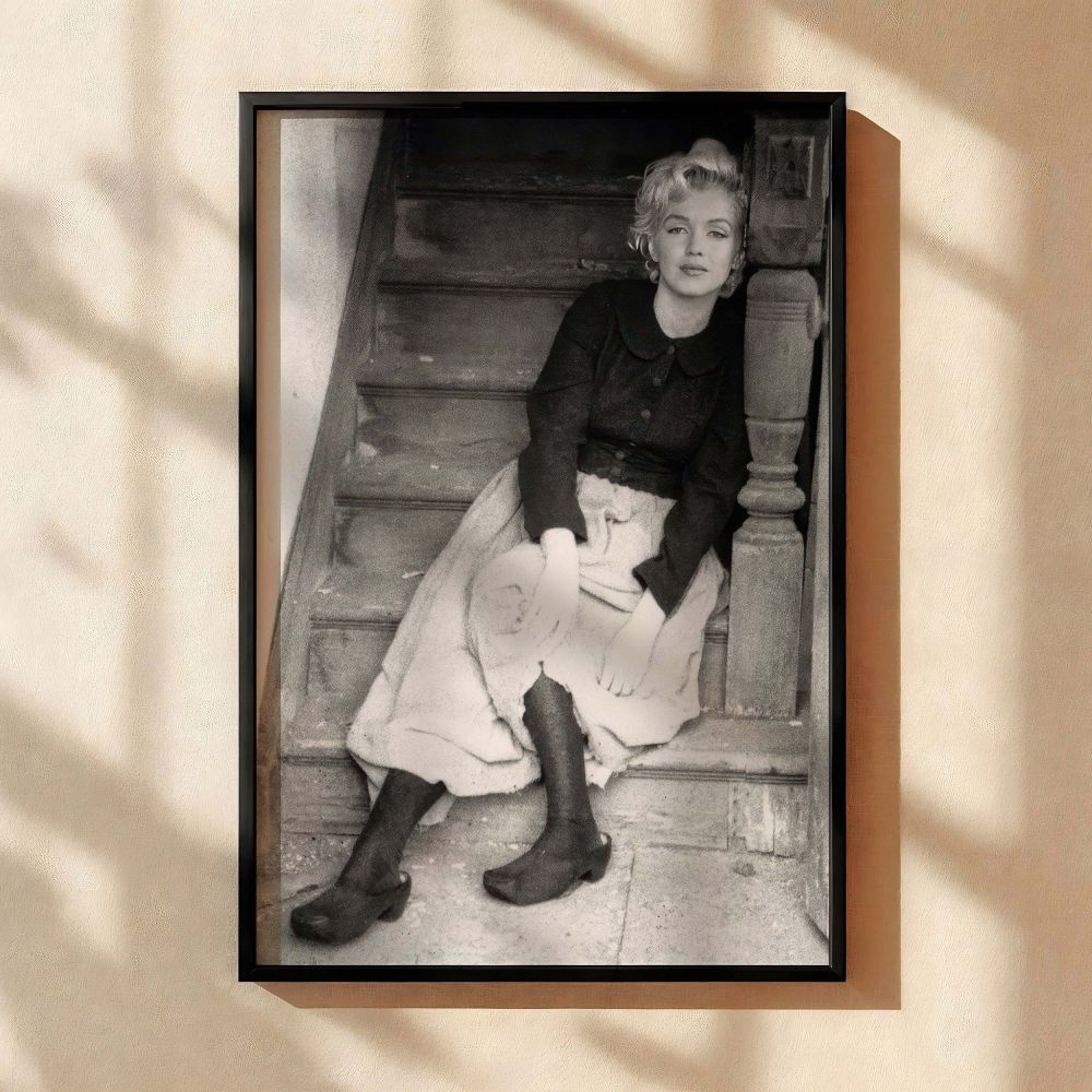 A quiet and graceful Marilyn Monroe sits on an aged wooden staircase in this striking black and white photo print capturing the raw charm of the film legend in a vintage Hollywood moment perfect for nostalgic home or gallery wall decor.