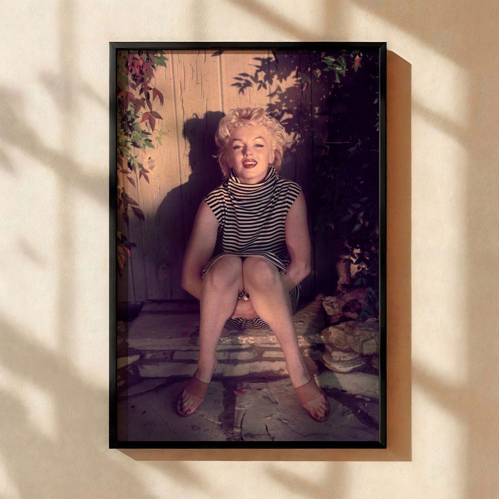 This soft-toned image of Marilyn Monroe showcases her in a classic striped sleeveless dress sitting casually on stone steps with a dreamy expression perfect for vintage wall art lovers and retro Hollywood decor collectors who appreciate timeless beauty an