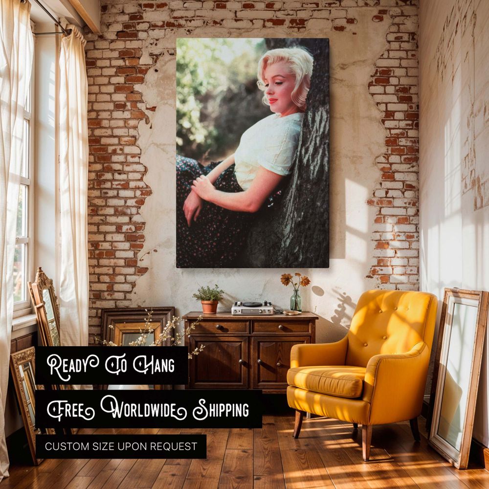 This Marilyn Monroe canvas print captures the legendary actress in a thoughtful pose wearing a floral skirt and white blouse while sitting against a tree surrounded by nature evoking timeless Hollywood glamour and vintage wall art appeal for lovers of cla