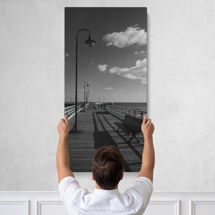 Black and white empty seaside pier with benches and lamps canvas print, tall canvas held against a wall