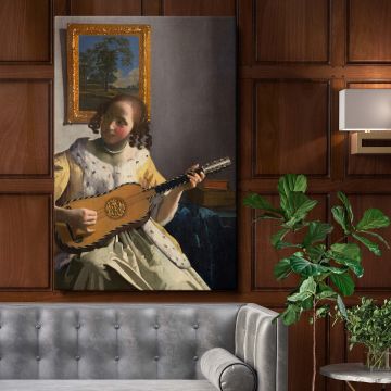 Wall canvas featuring Johannes Vermeer's The Guitar Player showing a young woman in elegant yellow attire strumming a guitar in a softly lit interior, with intricate details of her dress, the guitar, and a framed landscape painting in the background.