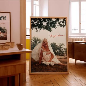 This Monroe wall print showcases her elegance and playfulness in a white dress sitting on the grass in an outdoor scene great for retro decor bridal-themed prints and collectors of classic film era photographs looking for unique portraits.
